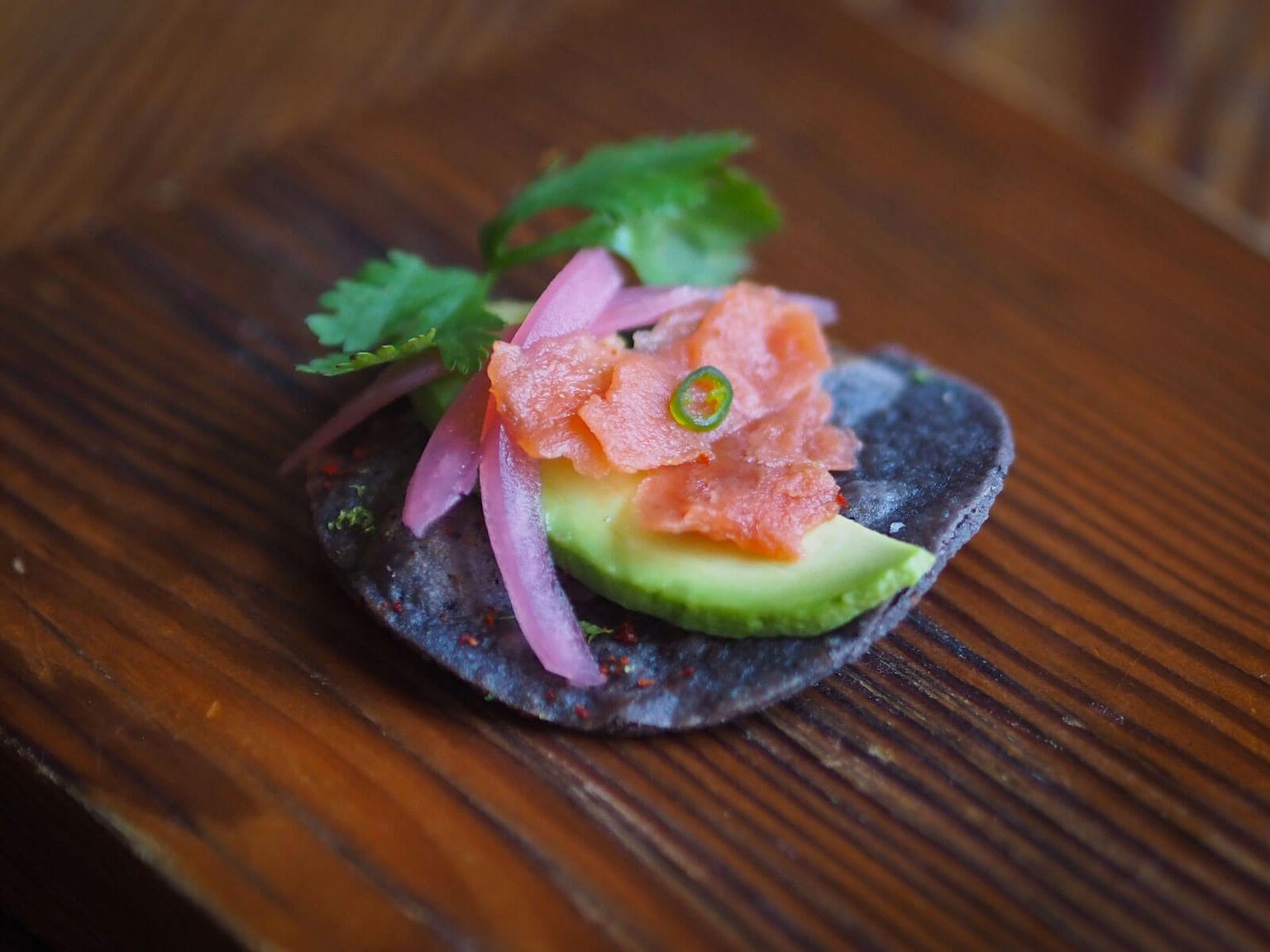 Blue corn chip with salmon, avocado and pickled red onion on top